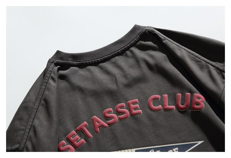 Close-up of a charcoal T-shirt back with raised red “SETASSE CLUB” lettering and part of a printed graphic.