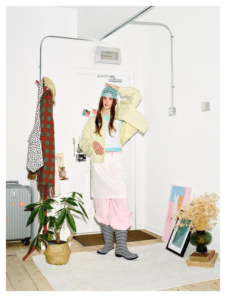 Model wearing a pale yellow cropped jacket over a white top, pink trousers, striped socks and black boots.