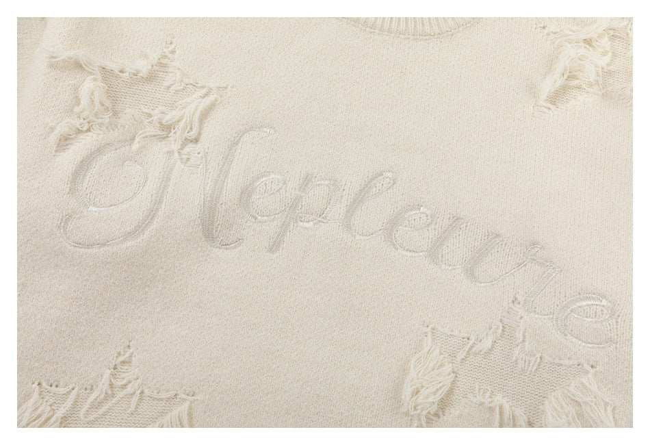 Close-up of raised script embroidery and distressed knit patches on an ivory sweater.