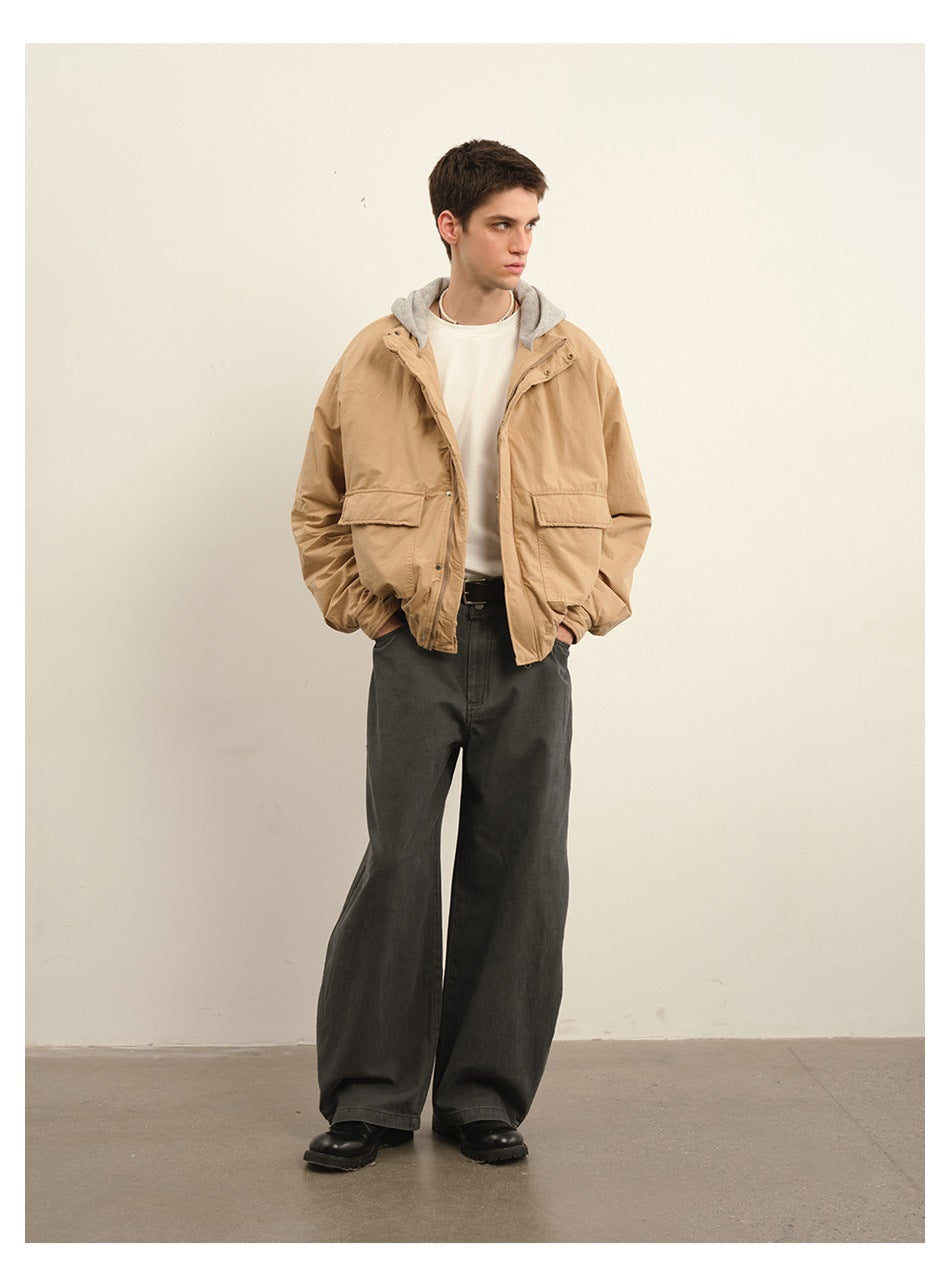 Full-length model wearing a tan hooded jacket with flap pockets, wide charcoal trousers and black shoes.