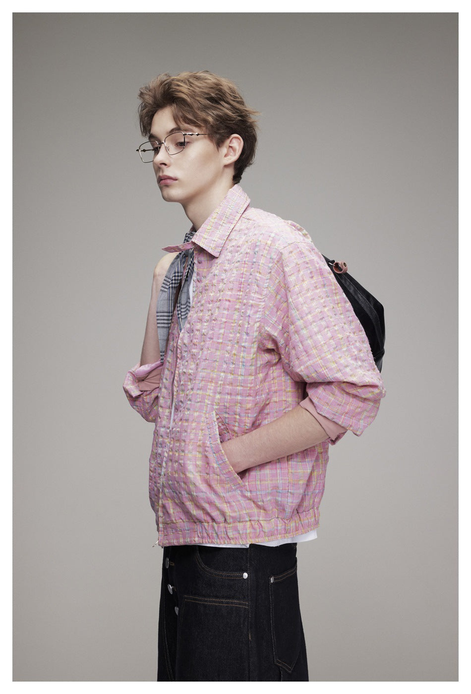Side view of a model wearing a pink plaid jacket with rolled cuffs over a white shirt and a gray neck scarf.