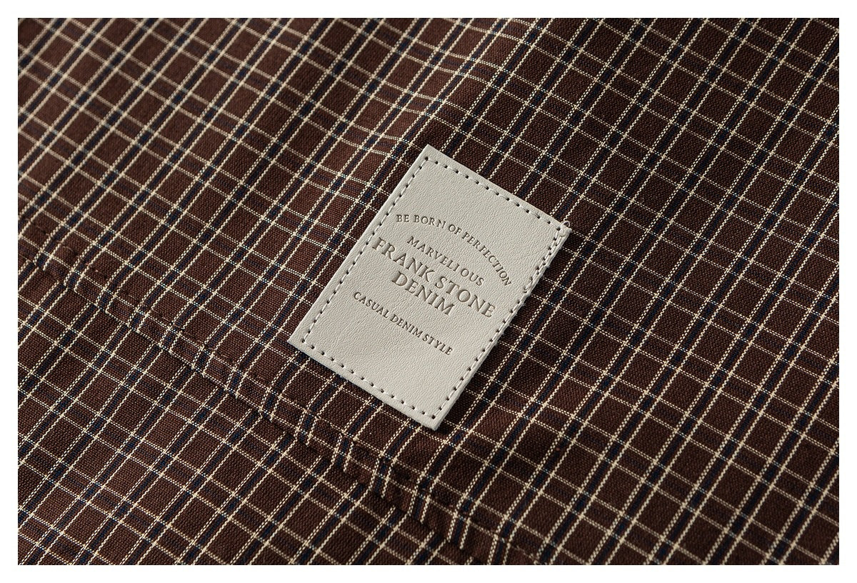 Close-up of a cream-colored sewn label on brown plaid fabric.
