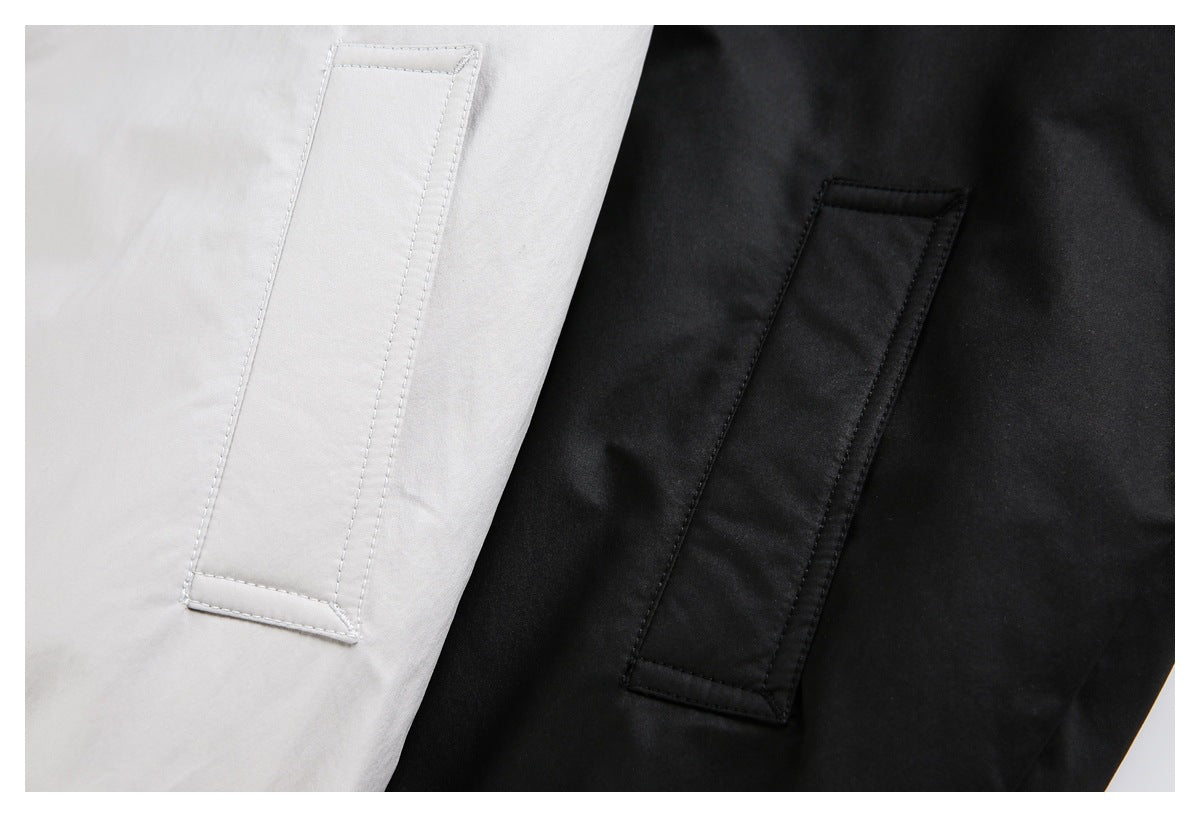 Close-up of long rectangular welt pockets on light gray and black jacket fabric.