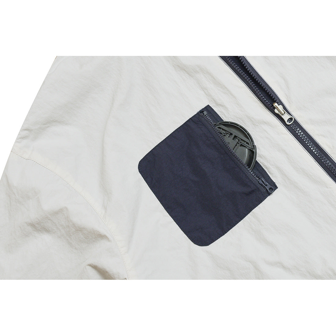 Close-up of a pale jacket panel with a navy zip pocket and a round black item tucked inside.