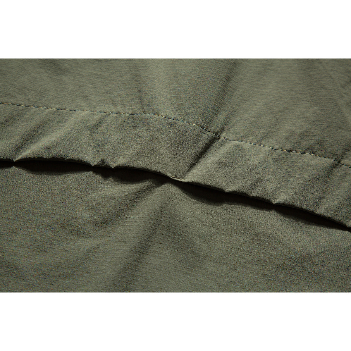 Close-up of the olive garment's stitched hem and overlapping fabric panels.