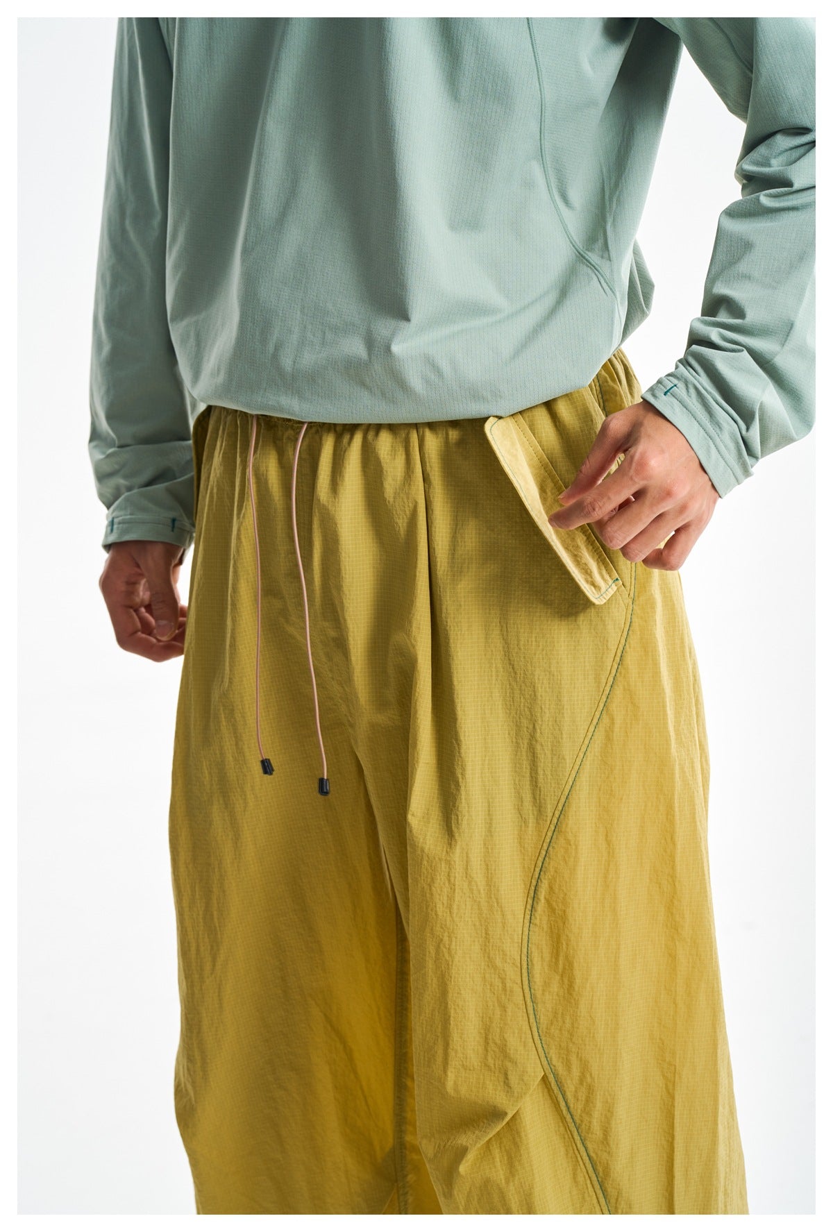 Close-up of mustard-yellow pants with a drawstring waist and curved side pocket, worn with a pale green top.