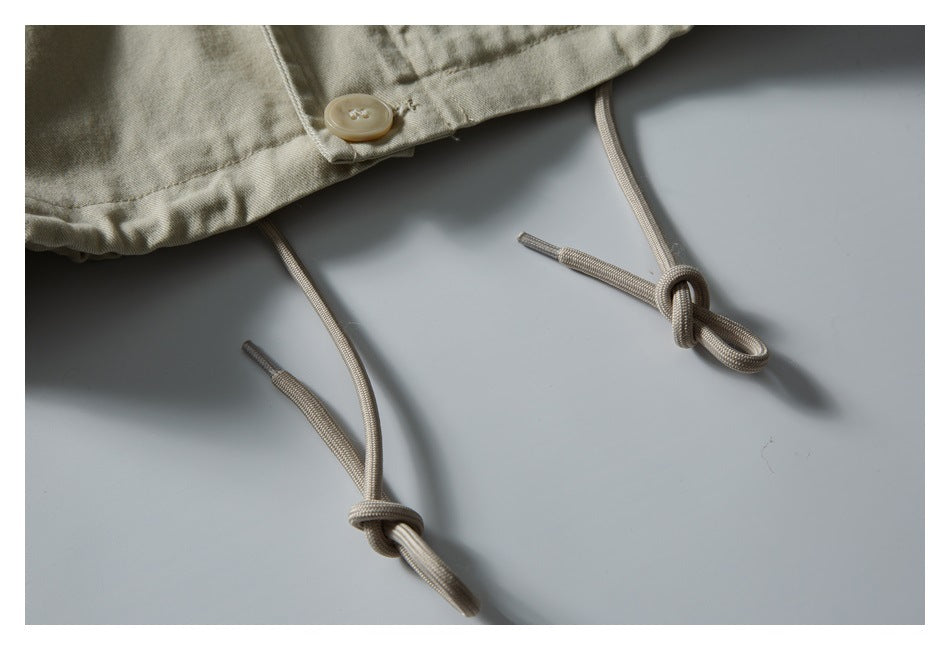 Close-up of light beige jacket hem with adjustable drawcords and a button.