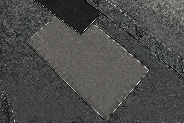 Close-up of a rectangular gray patch pocket with white stitching on a charcoal shirt beside its button placket.