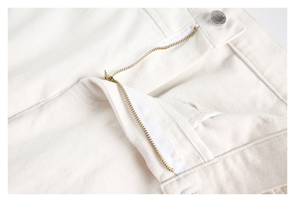 Close-up of ivory trousers with the fly open, showing the gold zipper, inner fastening, and waistband button.