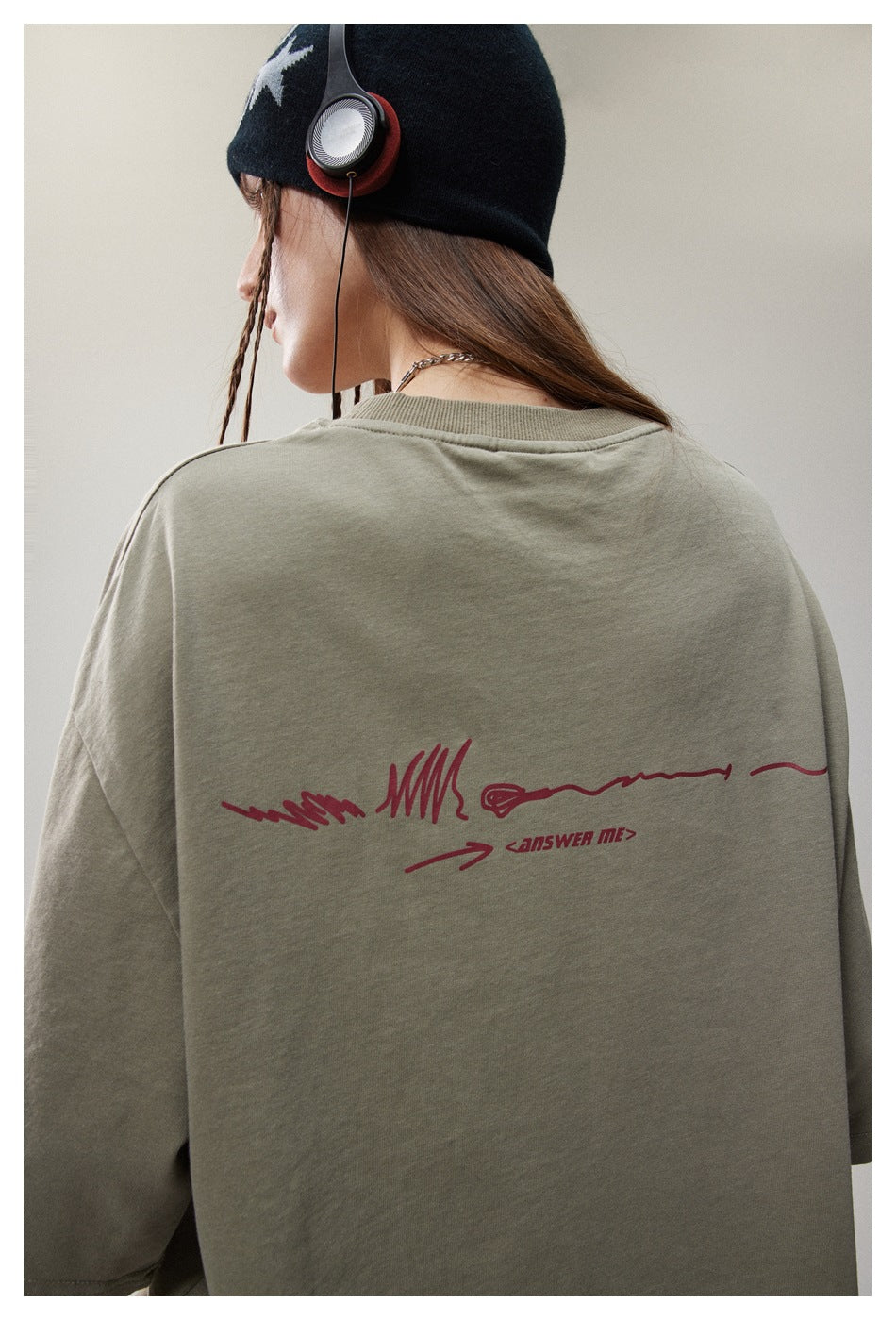 Close rear view of a sage-green T-shirt with a burgundy abstract graphic and lettering across the back.