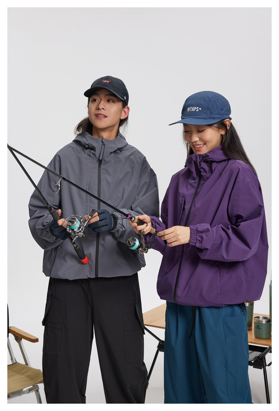 Two people wear hooded jackets in gray and purple while holding fishing rods.