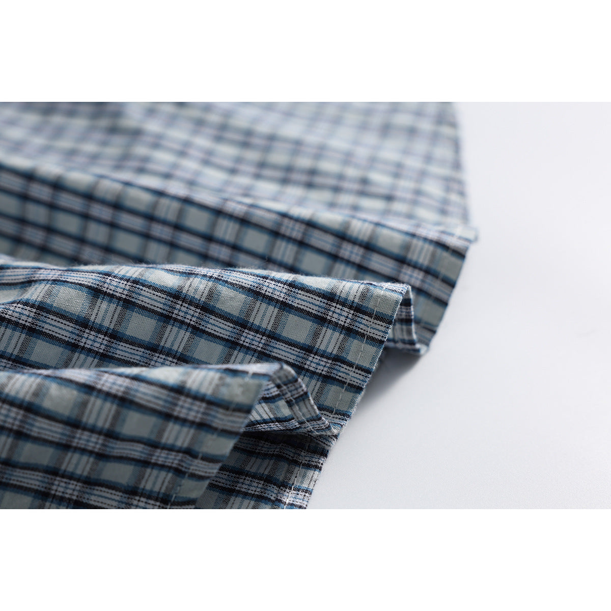 Close-up of folded blue, gray, and white plaid shirt fabric showing its pattern and edges.