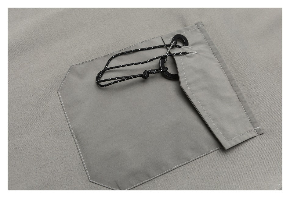 Close-up of a gray shirt pocket with a flap and black cord loop and hardware.