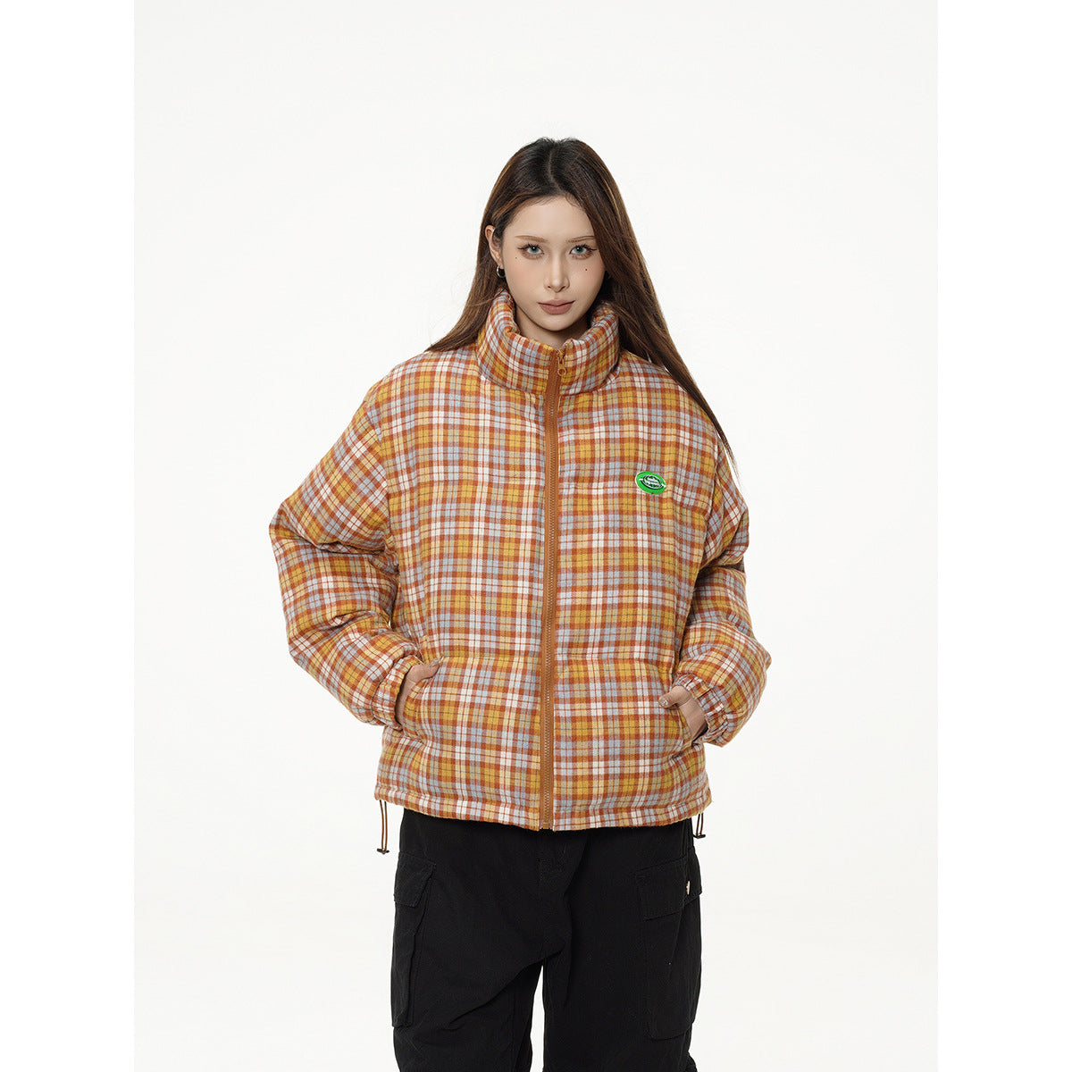 Model wearing an orange, cream, and brown plaid puffer jacket with a high collar and front zipper.
