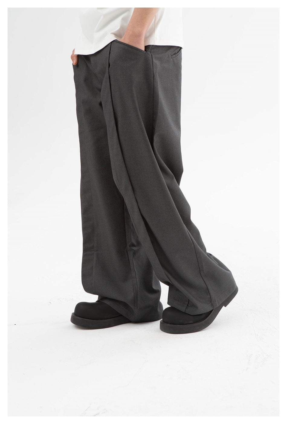 Close side view of loose charcoal-gray trousers worn with a white shirt, highlighting the wide legs and pockets.