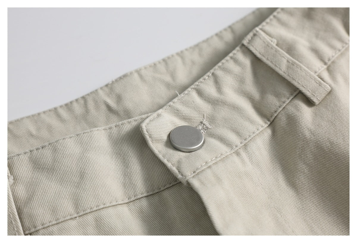 Close-up of light beige trousers showing the waistband, a silver button and a belt loop.