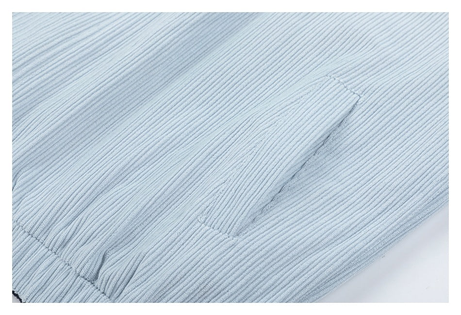 Close-up of a light blue ribbed corduroy garment showing a stitched pocket opening.