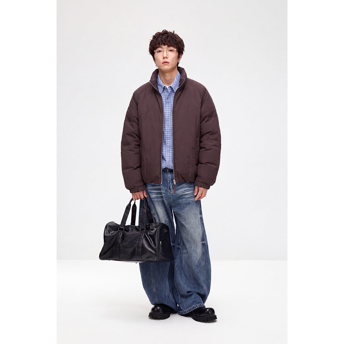 Model wearing a dark plum zip-front jacket with a stand collar, blue checked shirt and loose blue jeans.