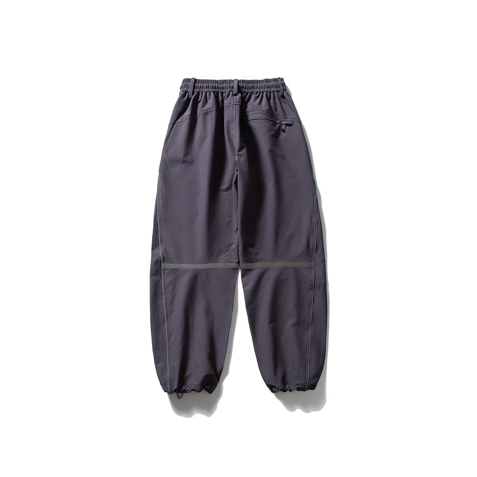 Dark charcoal loose-fit pants shown from the back, with an elastic waist, zip pocket, reflective knee bands and gathered