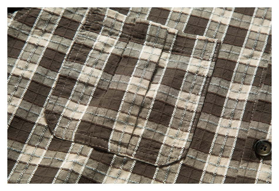 Close-up of a stitched chest pocket on brown, beige and gray plaid shirt fabric, with a dark button at the edge.