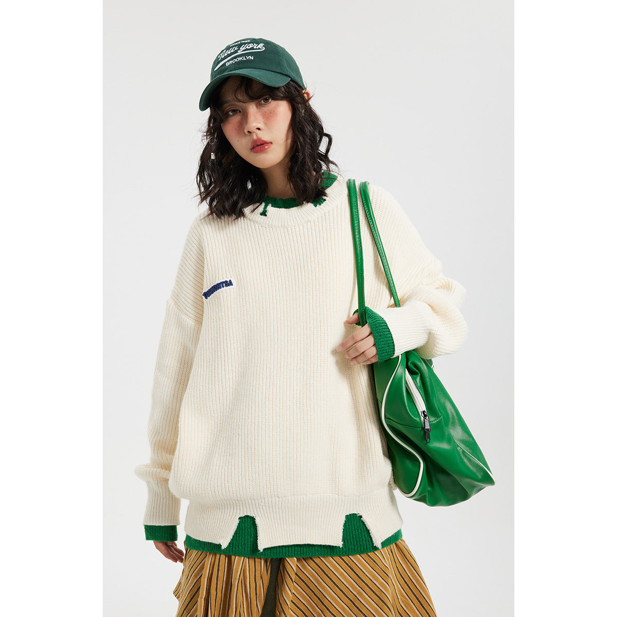 Model wearing an oversized ivory rib-knit sweater with green collar, cuffs and hem accents.