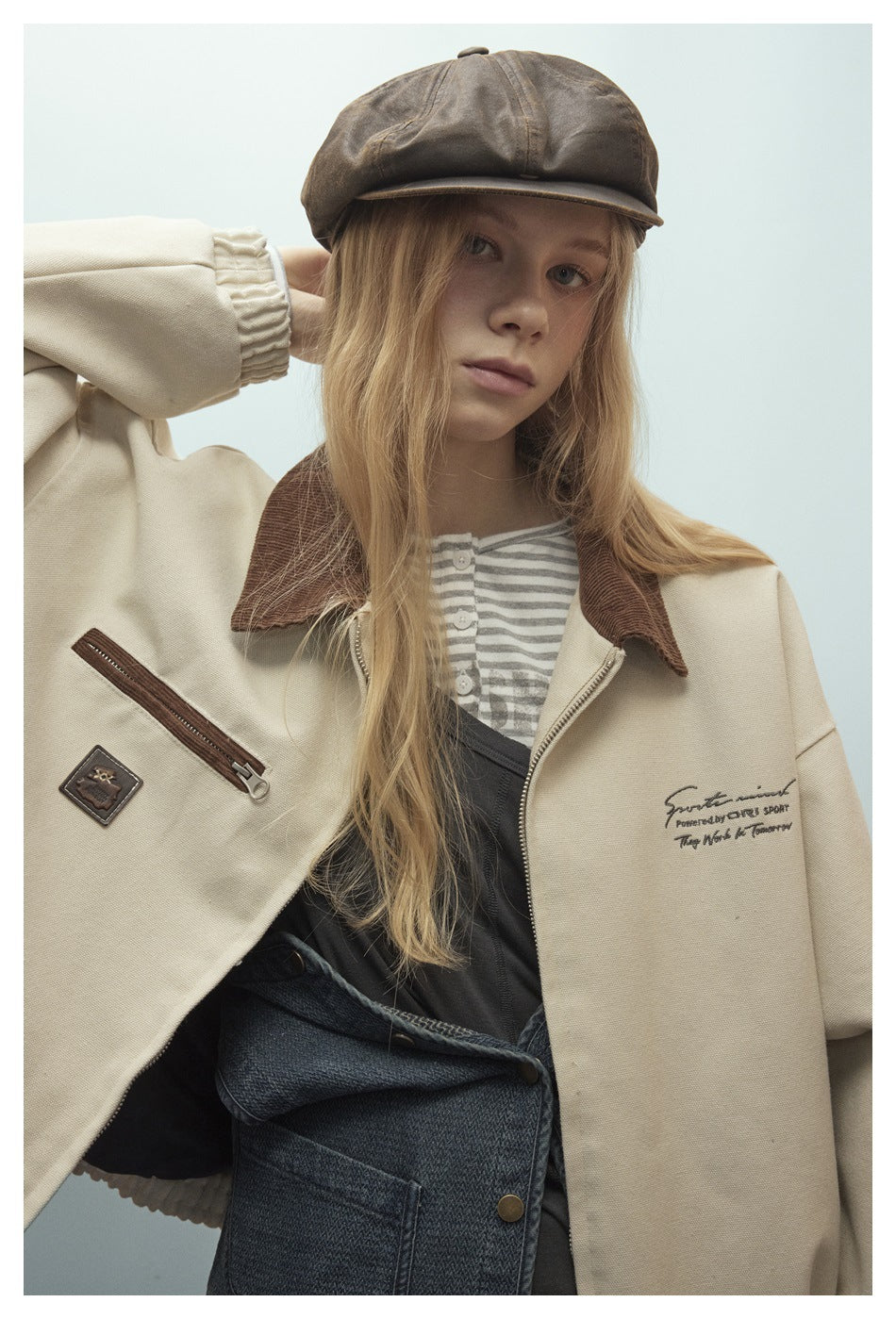 Close view of a model in a cream jacket with a brown corduroy collar, zip pocket and small chest lettering.