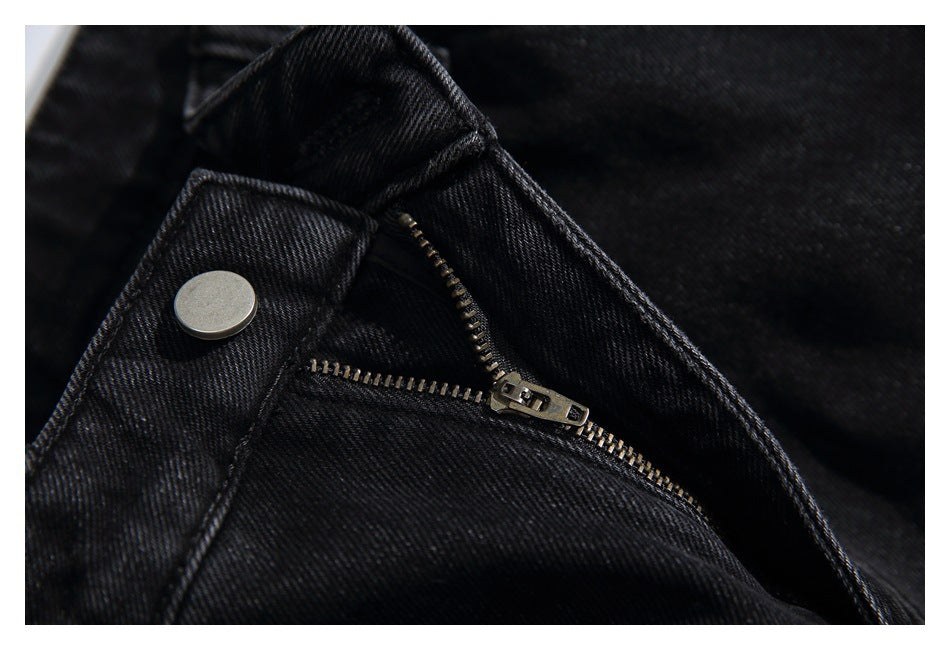 Close-up of black jeans showing the metal waist button and partly open zipper fly.