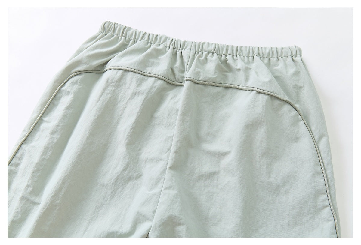 Back view of pale sage-gray pants showing the elastic waistband, center seam, and curved piping.