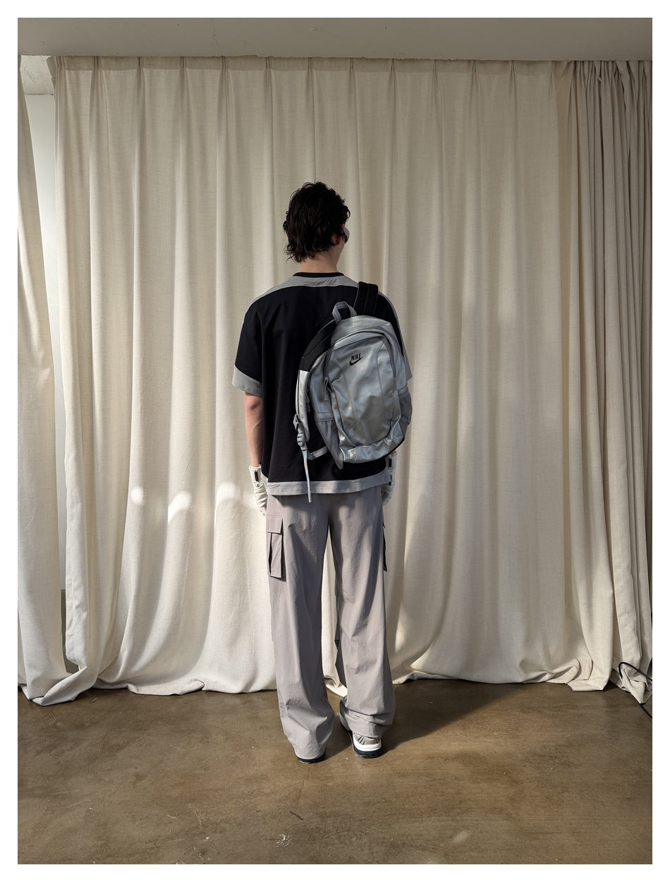 Back view of model in the black T-shirt with gray trim, gray cargo pants and a silver backpack covering the back