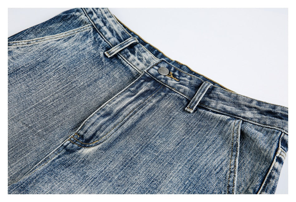 Close-up of faded blue jeans showing the waistband, metal button, belt loops and curved pocket stitching.