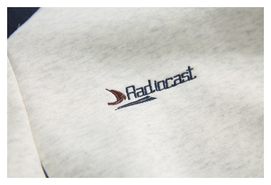 Close-up of embroidered English lettering and a small sail-like motif on the light gray sweatshirt.