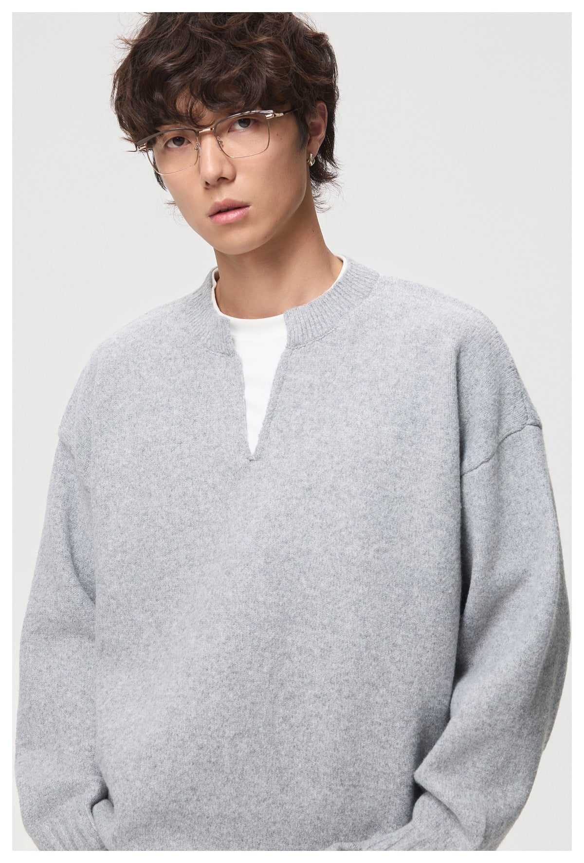 Close-up of a model wearing a light gray oversized sweater with a ribbed split neckline.