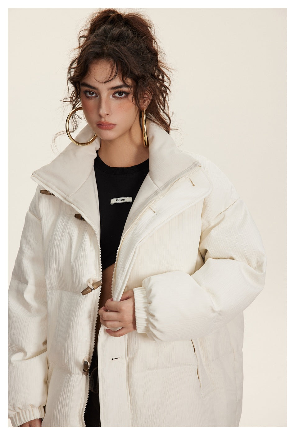 Model wearing an open ivory quilted puffer jacket with a high collar, toggle closures, and oversized sleeves.