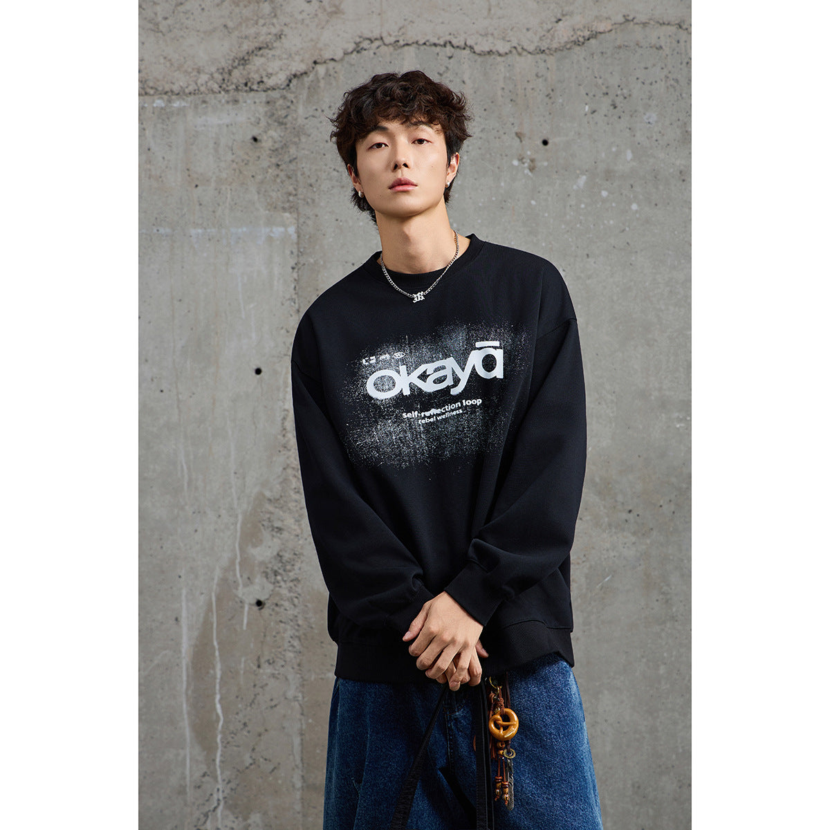 Model wearing a black oversized crewneck sweatshirt with a large white distressed graphic on the front.