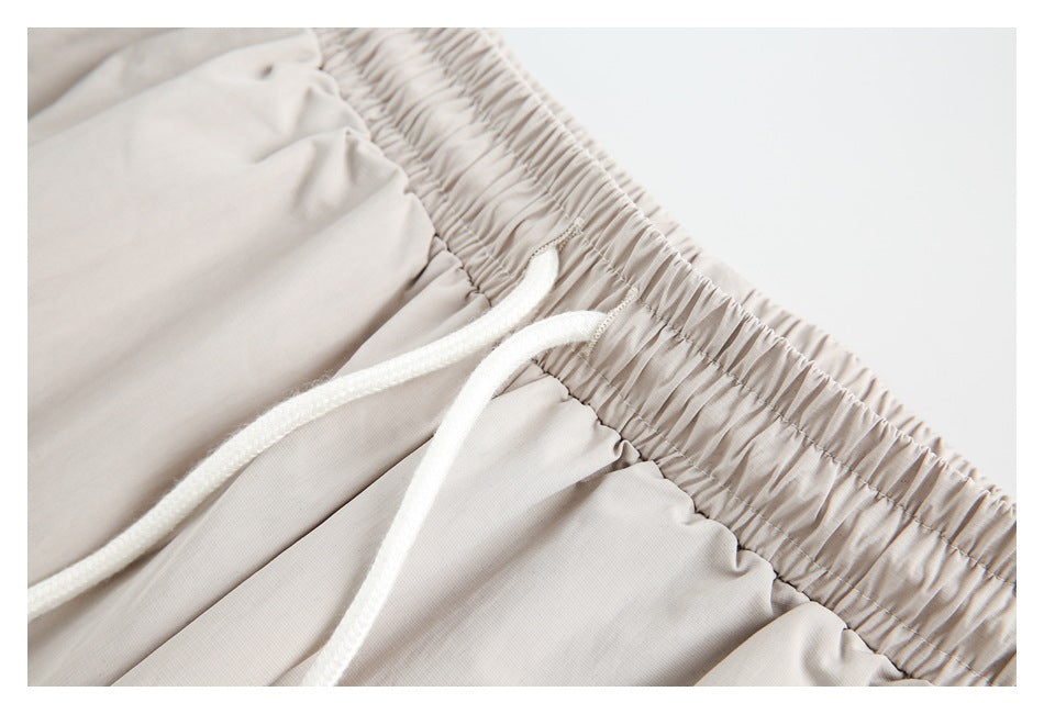 Close-up showing the gathered elastic waistband and white drawstrings on beige pants.