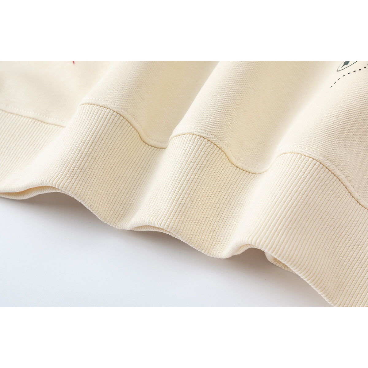 Close-up of the cream sweatshirt's ribbed hem and stitched seam.