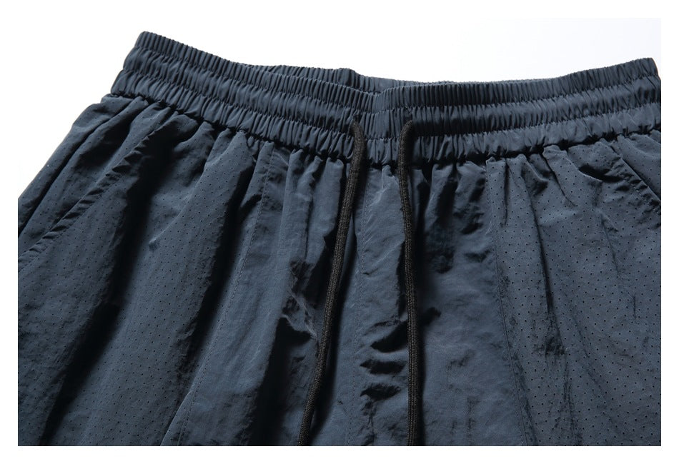 Close-up of navy shorts showing the gathered elastic waistband, drawcords, and perforated fabric panels.