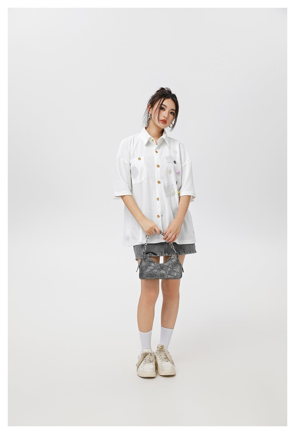 Model wearing a white oversized short-sleeve button-front shirt with grid-stitched pockets and decorative buttons.
