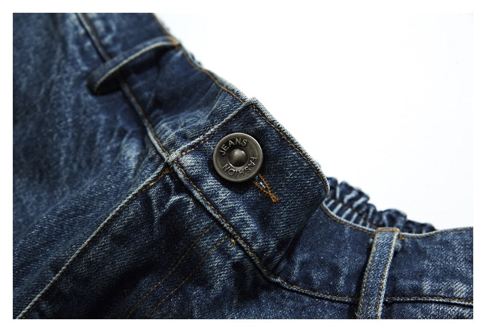 Close-up of a metal button engraved with English lettering on dark blue denim trousers.