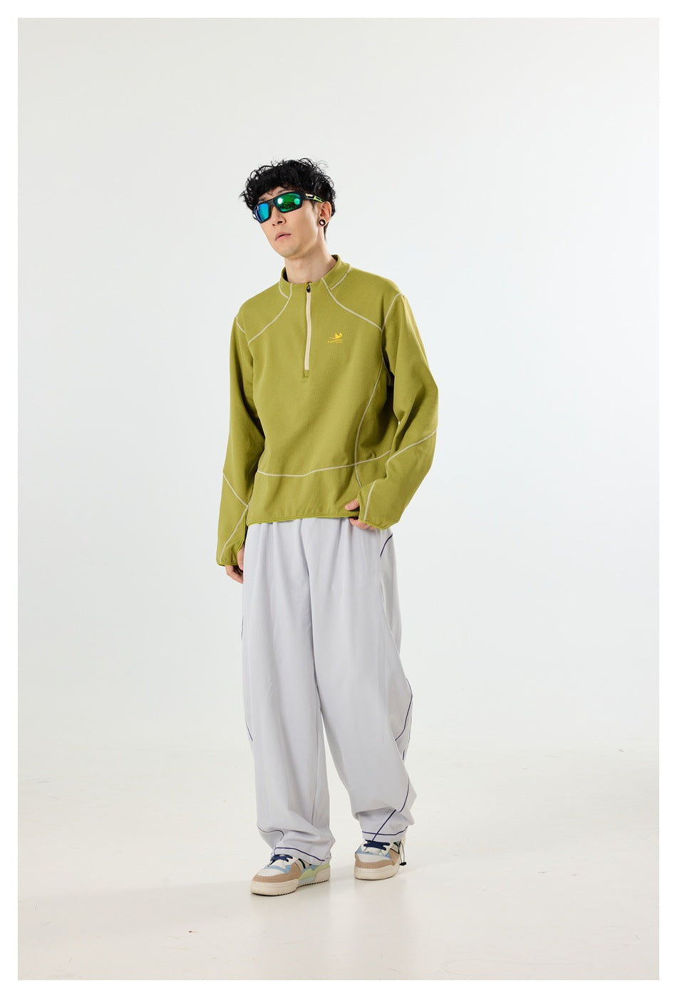 Model wearing an olive quarter-zip pullover with contrast seams and loose light-gray trousers, in a three-quarter pose.