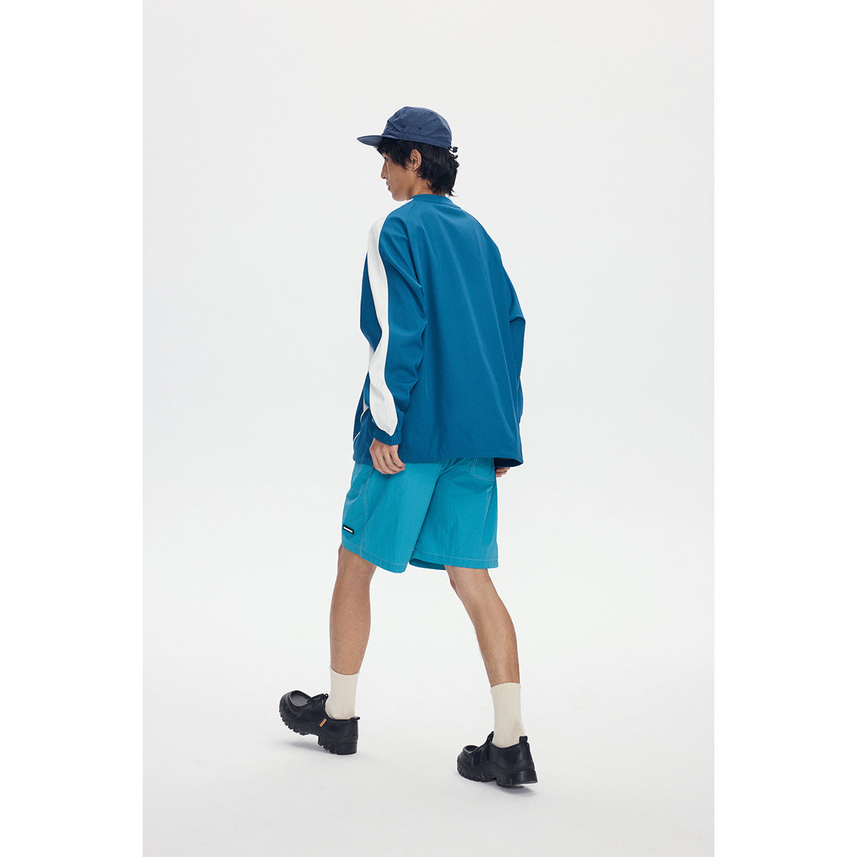 Rear view of a model wearing a blue-green pullover with white sleeve panels and matching teal shorts.