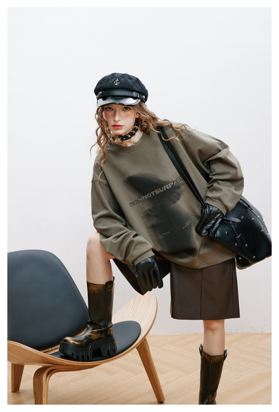 Close view of a model wearing an olive-gray oversized graphic sweatshirt and carrying a black studded tote.