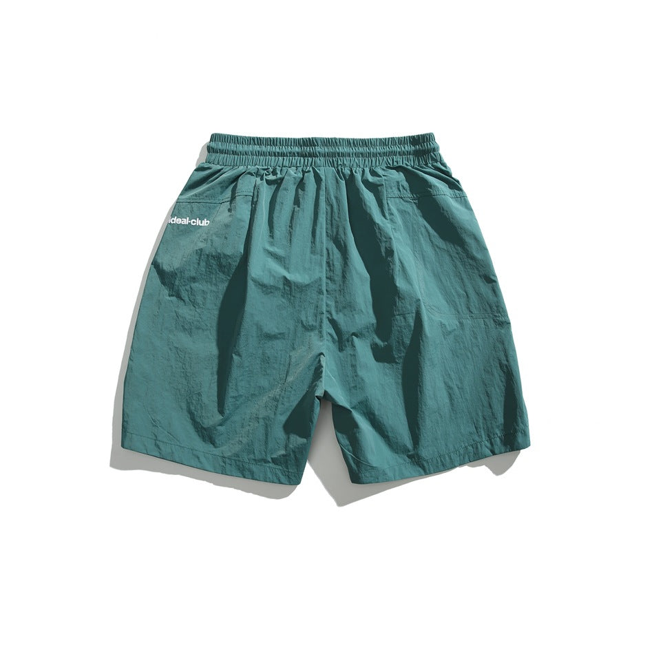 Back view of teal shorts with an elastic waistband, side pockets, and a small white logo.
