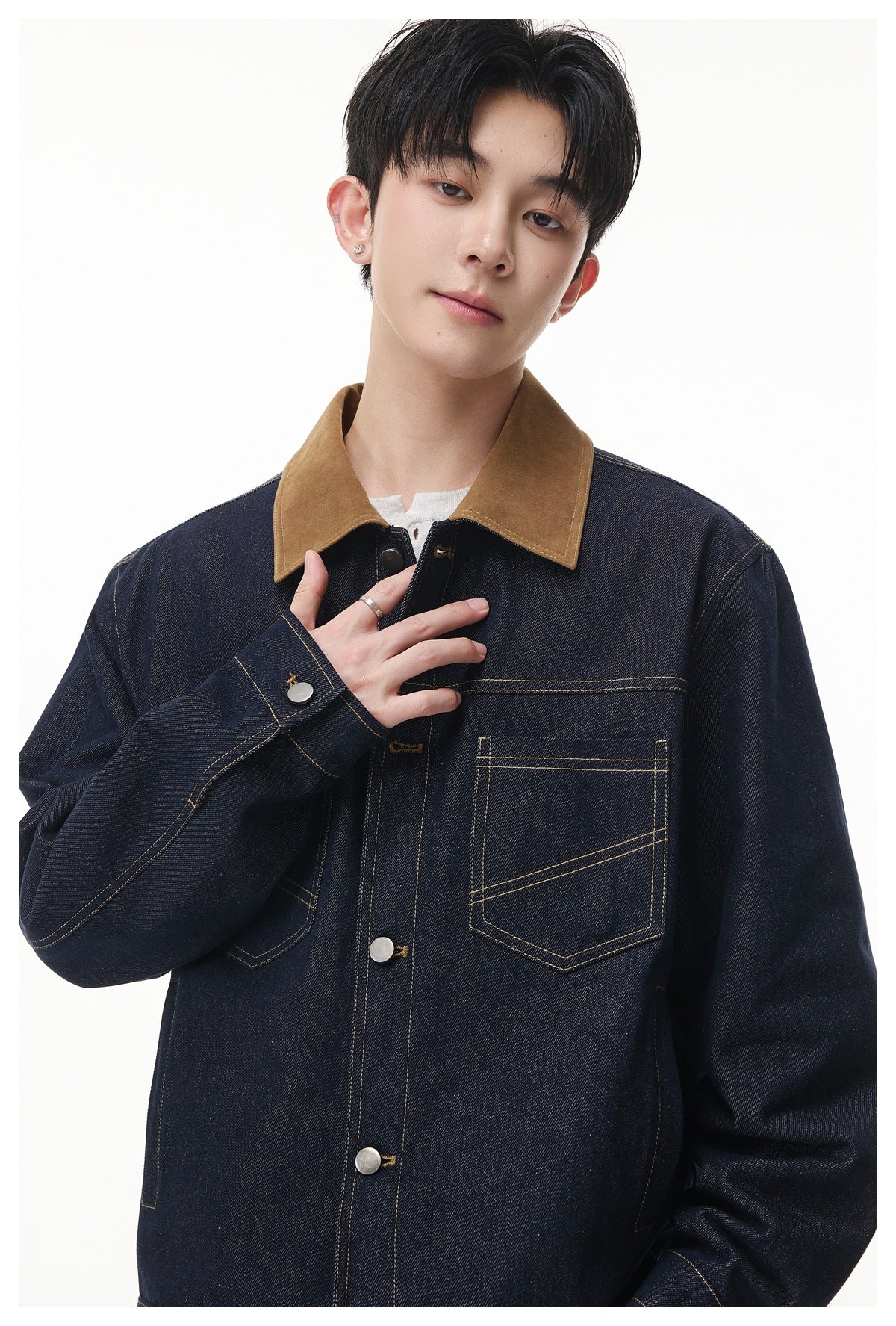 Close front view of a model wearing a dark indigo denim jacket with a brown collar and contrast stitching.