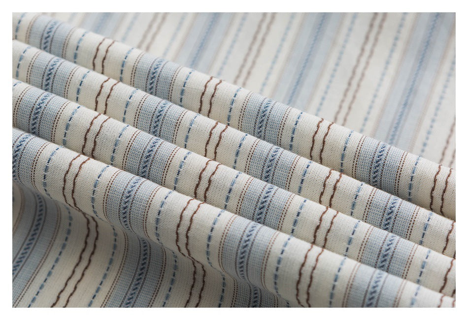 Close-up of cream woven fabric with narrow blue, gray, and brown stripe patterns.