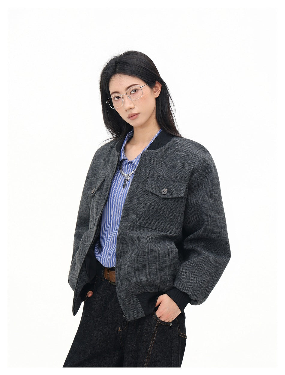 Model wearing a charcoal gray plaid bomber jacket with black ribbed collar and cuffs, open over a blue striped shirt.