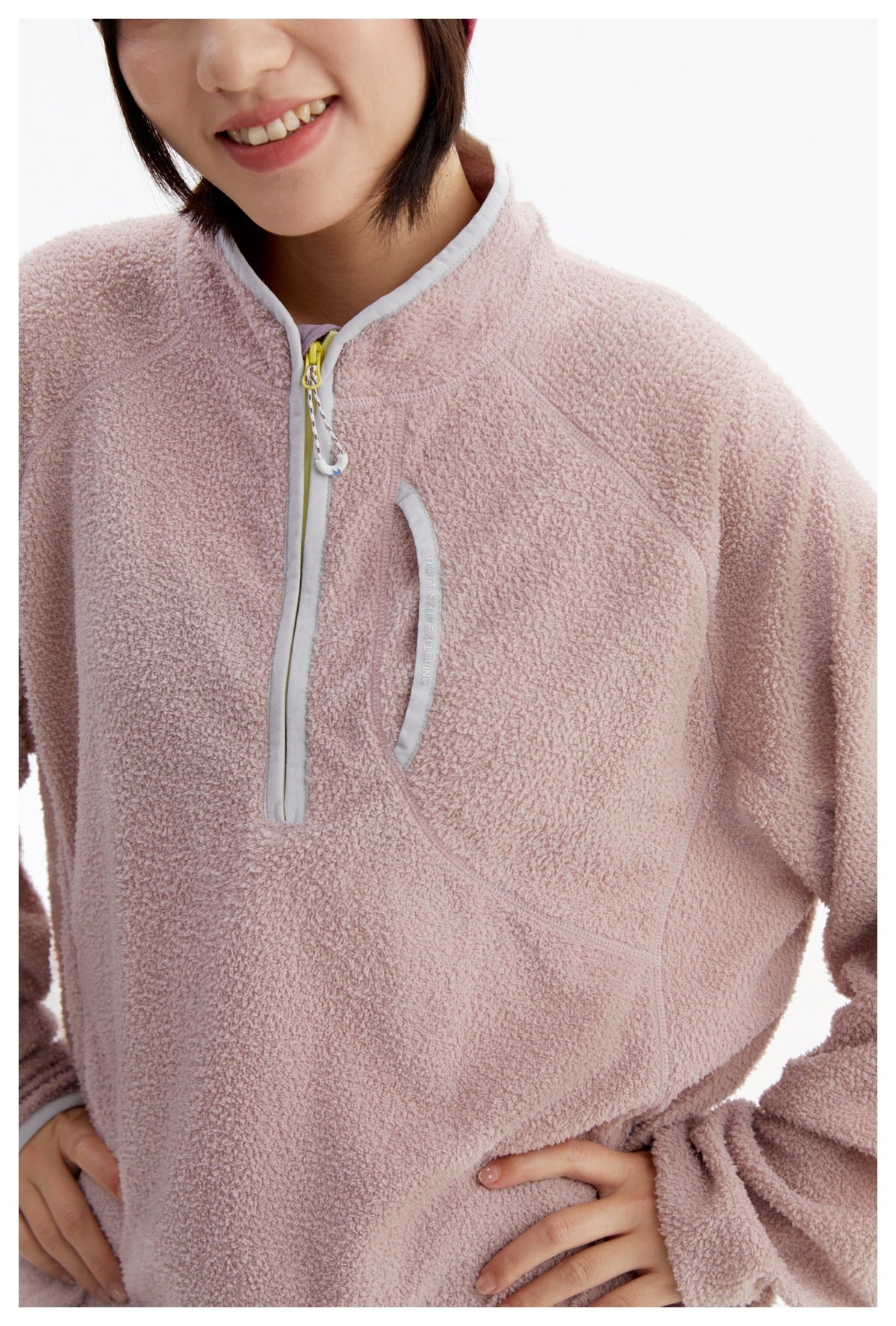 Close-up of the pink fleece pullover's textured front, short zipper, and curved chest pocket.