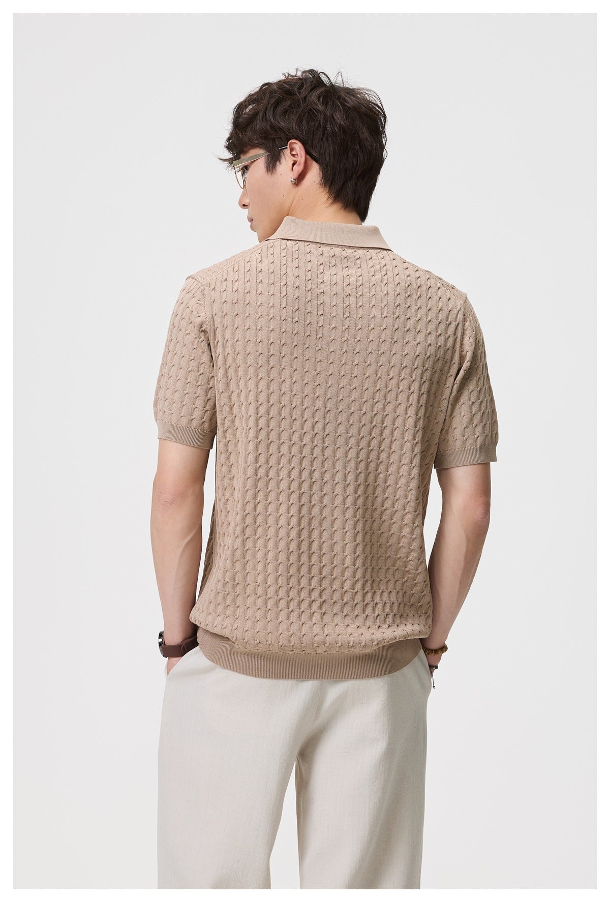 Back view of man wearing camel cable-knit short-sleeve polo with cream trousers