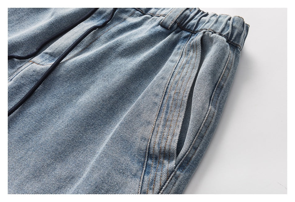 Close-up of light blue washed denim pants showing the gathered elastic waistband, dark drawstring, and stitched side pocket.