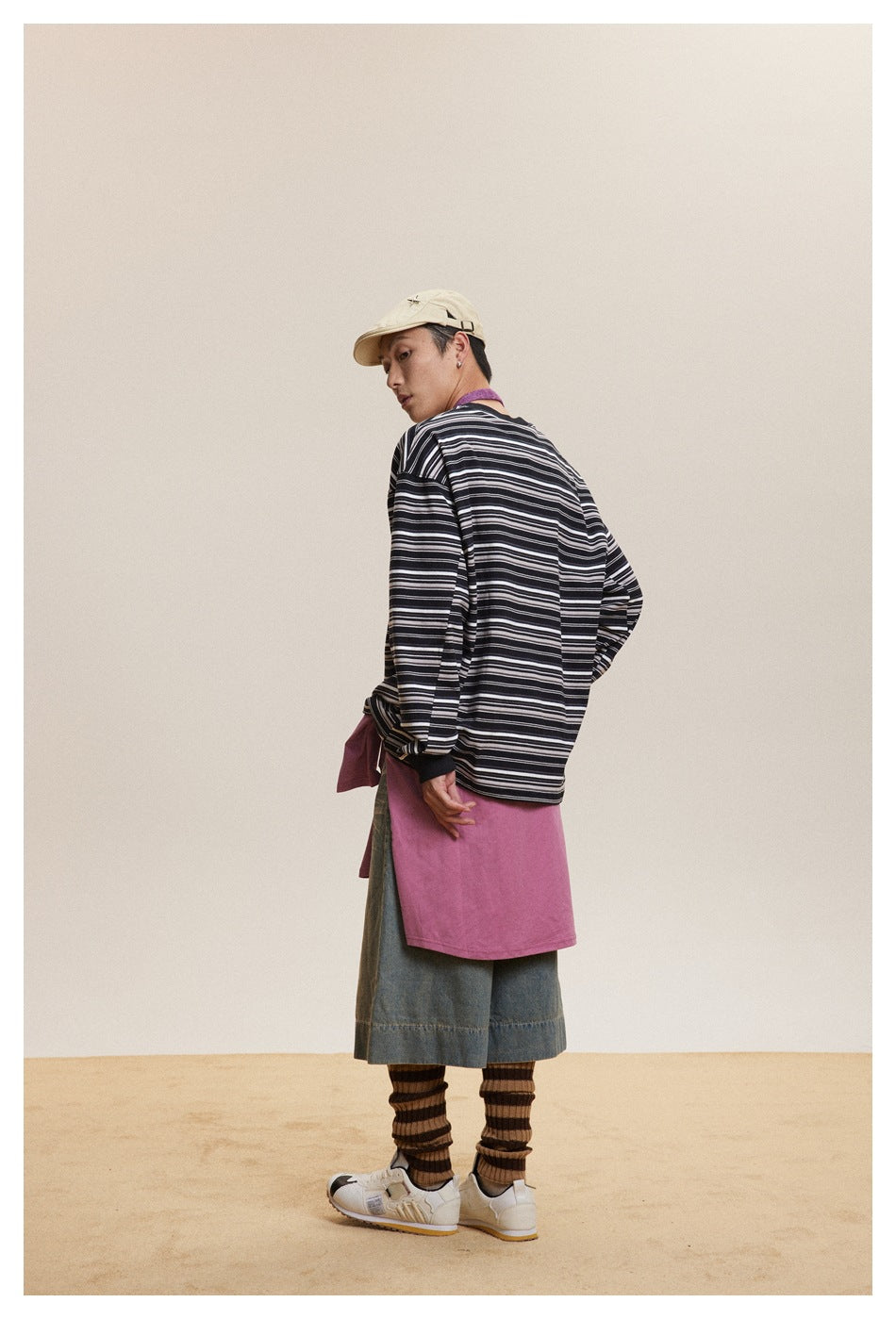 Model turned away wearing the black striped long-sleeve top with a pink layer, denim shorts and striped leg warmers